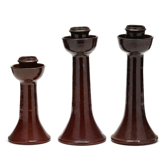 A trio of dark brown ceramic candlesticks arranged in ascending height against a stark white background.