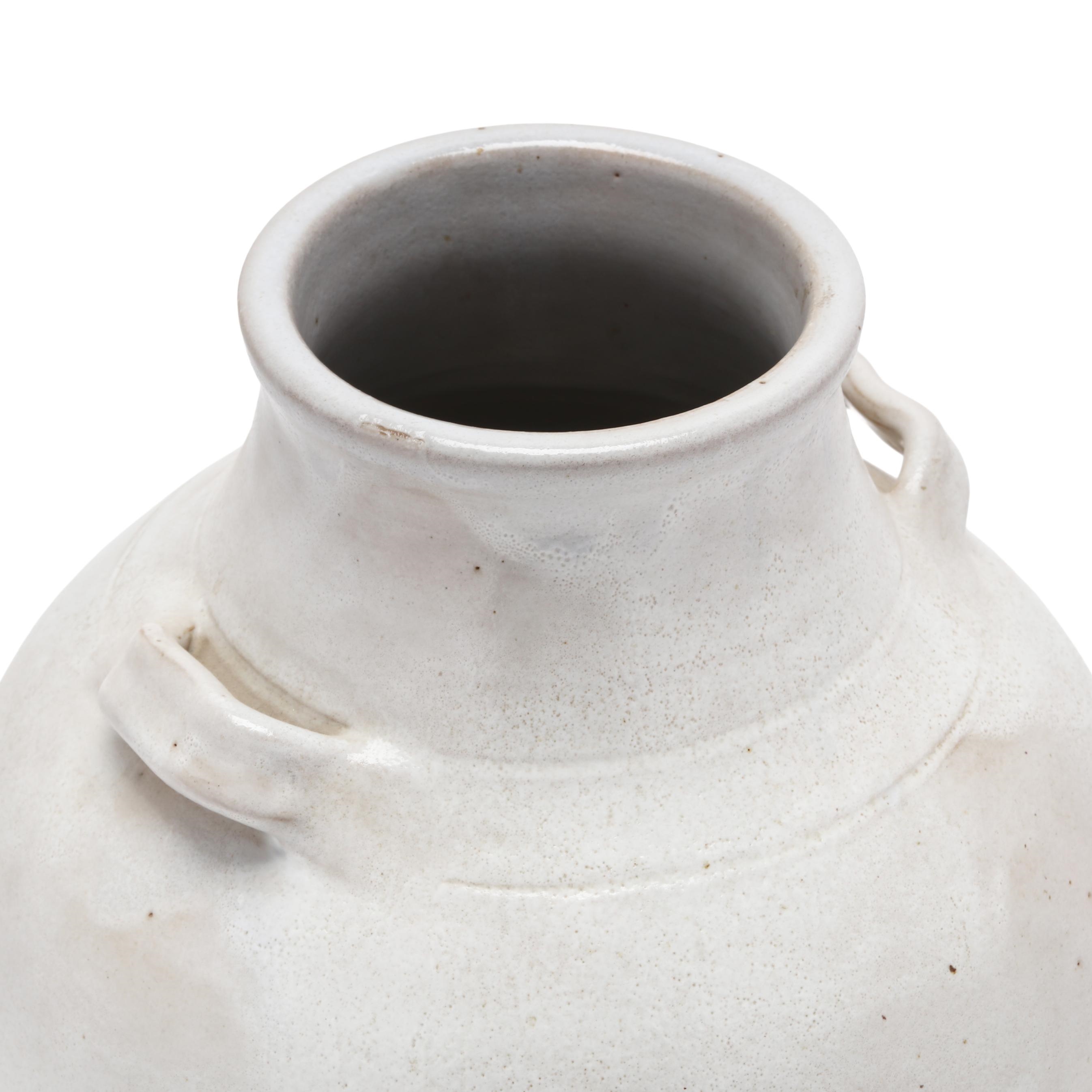 A white ceramic vase with a rounded body and small handles, resting on an exposed terracotta base.