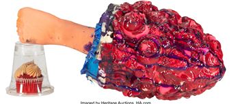 A surreal sculpture featuring a fleshy, brain-like mass with a human arm reaching into a plastic cup containing a cupcake.