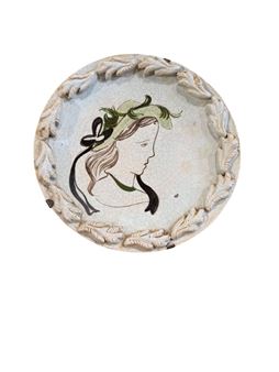 A profile portrait of a woman in profile on a circular ceramic plate with a leafy rim.