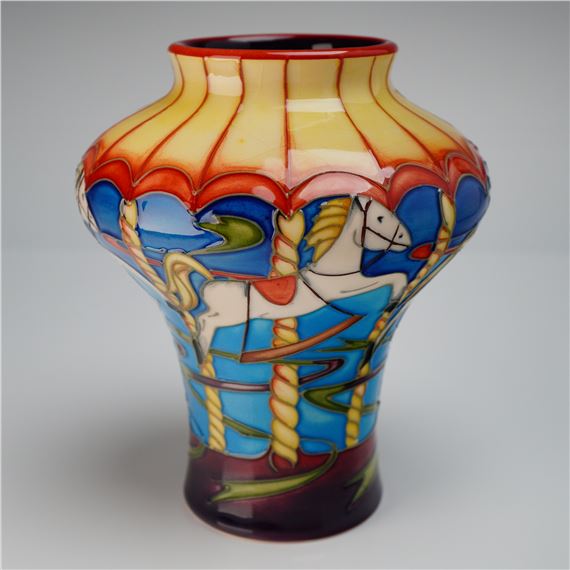 A colorful ceramic vase featuring a whimsical carousel scene with a white horse and vibrant striped canopy.