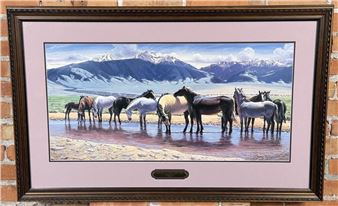 "A framed painting of a herd of horses drinking from a stream with mountains in the background."