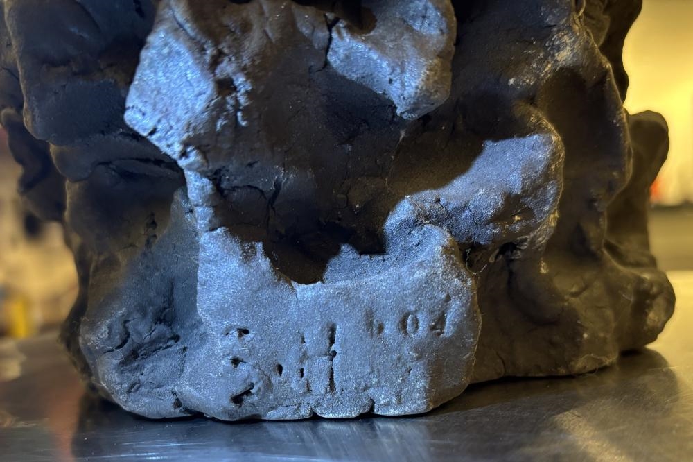 A dark, textured sculpture resembling a crumpled mass or organic form.