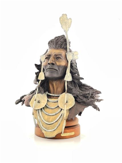 A sculpted bust of a figure with dark hair and ornate jewelry, featuring a feathered headdress and layered necklaces.