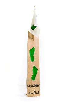 A vertical wooden sculpture featuring green footprints and a hanging white cloth.