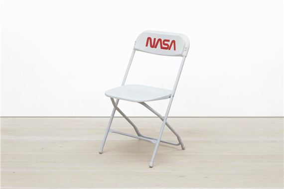 A minimalist white folding chair with a red logo on the backrest, set against a stark white background.