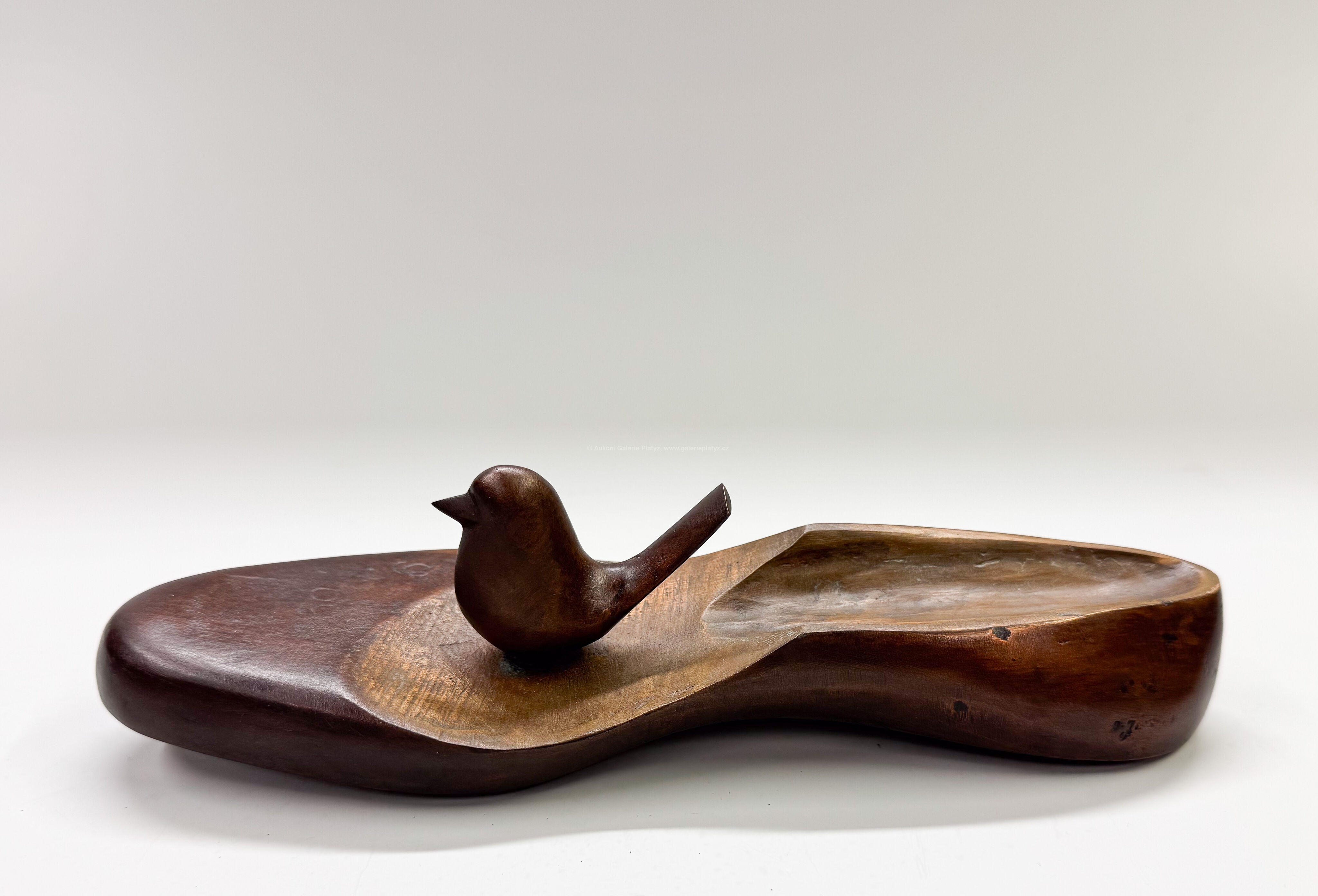 A wooden sculpture featuring a small bird perched on an irregular, boat-shaped base.