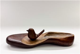 A wooden sculpture featuring a small bird perched on an irregular, boat-shaped base.