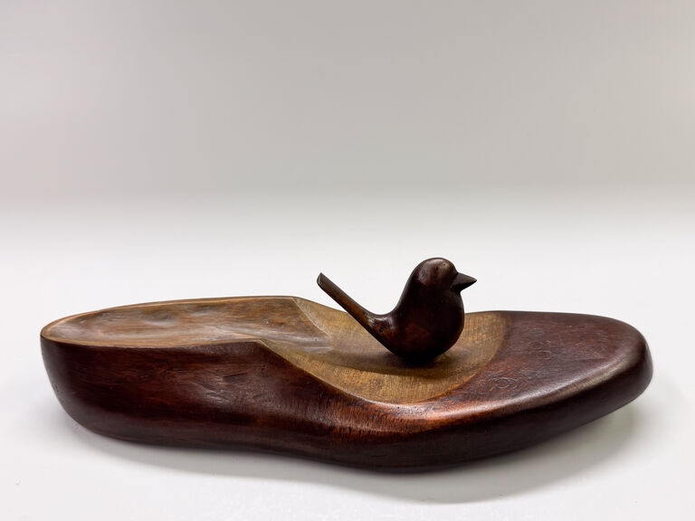 A wooden sculpture featuring a small bird perched on an irregular, boat-shaped base.