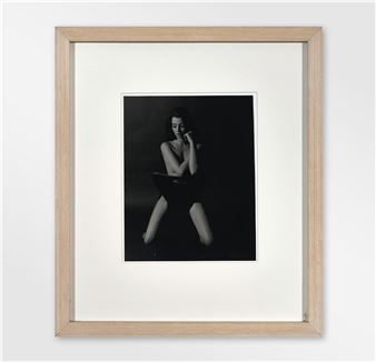 A framed black-and-white portrait of a seated figure in a dark studio setting.