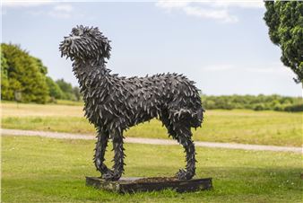 A spiky, dark sculpture of a dog standing in a grassy field.