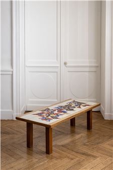 A wooden bench with a colorful abstract design on its seat placed in front of white paneled doors.