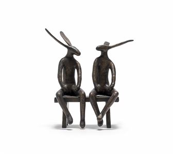 A bronze sculpture of two seated rabbit figures on a bench.