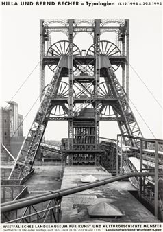 A black and white photograph of an industrial mining structure with large wheels.