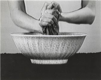 A black-and-white close-up of hands kneading dough inside a textured bowl.