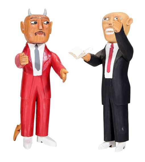 A wooden sculpture featuring two figures in suits, one with devil horns and the other holding a piece of paper.