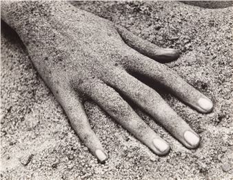 A monochromatic close-up of a hand resting on textured sand.