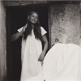 A black-and-white portrait of a person in a white nightgown standing in a doorway, holding their hair back.