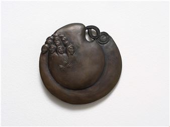 A bronze relief sculpture featuring a crescent moon shape with a cluster of small faces and an eye motif.