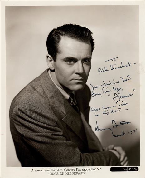 A black-and-white studio portrait of a man in a suit, signed with handwritten text.