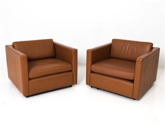 A pair of minimalist brown leather armchairs set against a stark white background.