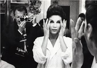 A black-and-white portrait captures a woman in a robe posing with hands to her face, surrounded by photographers.