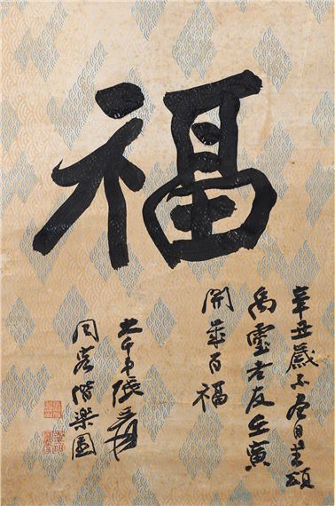 A vertical scroll featuring a large calligraphic character on patterned paper with smaller inscriptions and seals.