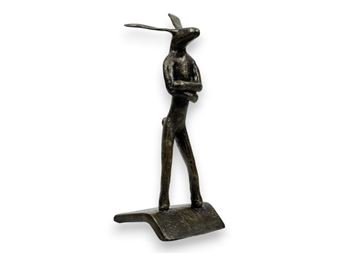 A bronze sculpture of a rabbit-like figure standing on a curved base.