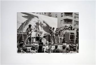 A black-and-white photograph capturing a live musical performance with a large eagle mural in the background.