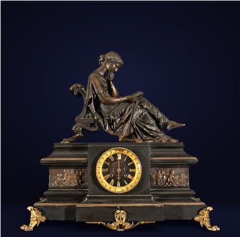 A classical bronze clock featuring a seated female figure reading, mounted on an ornate rectangular base with gold accents.