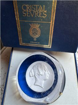 A blue glass paperweight with a white relief portrait of a woman's profile, displayed in its open box.
