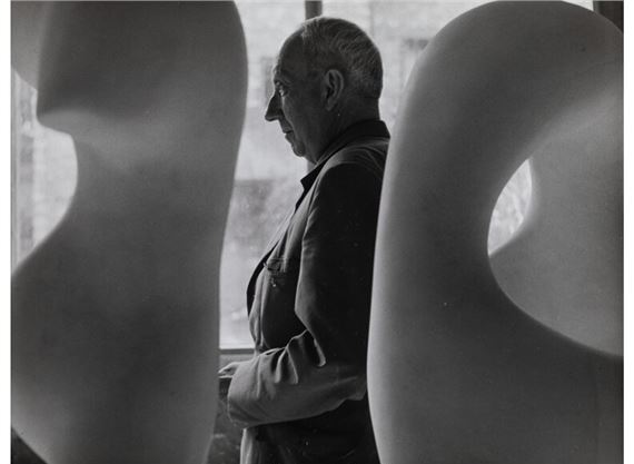 A black-and-white portrait of an older man framed by large, smooth sculptural forms.