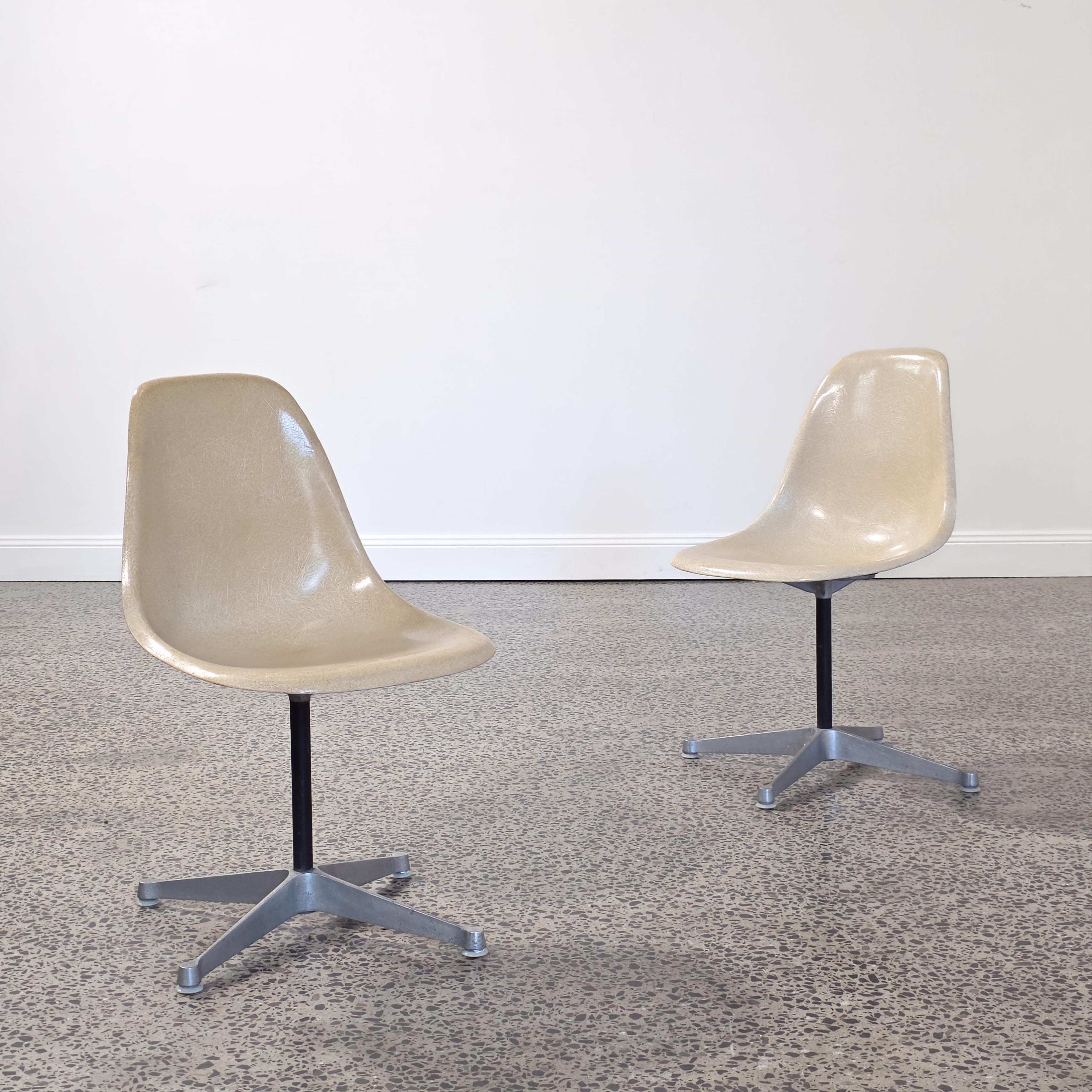 A pair of beige molded chairs on star-shaped bases against a plain wall.
