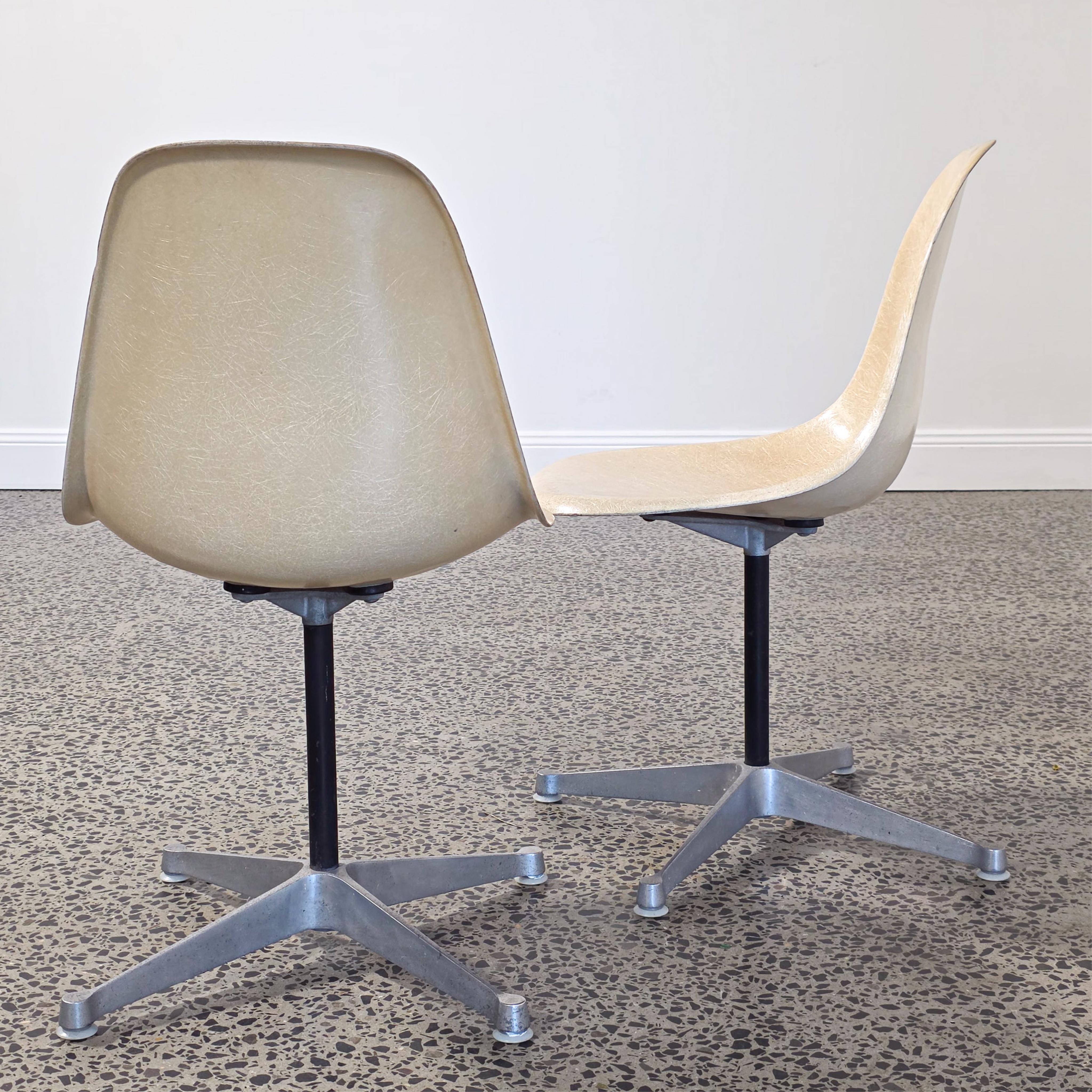 A pair of beige molded chairs on star-shaped bases against a plain wall.
