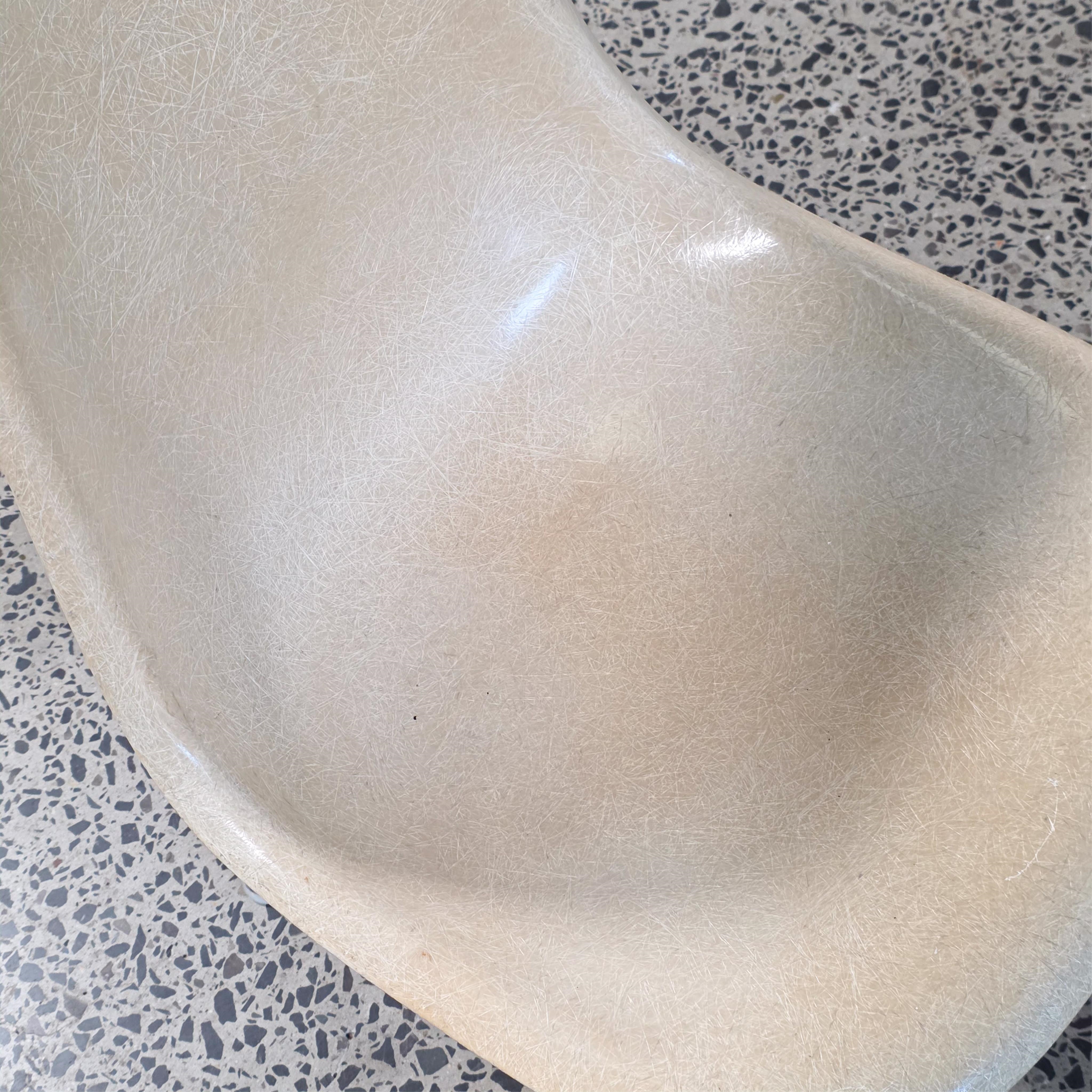 A pair of beige molded chairs on star-shaped bases against a plain wall.