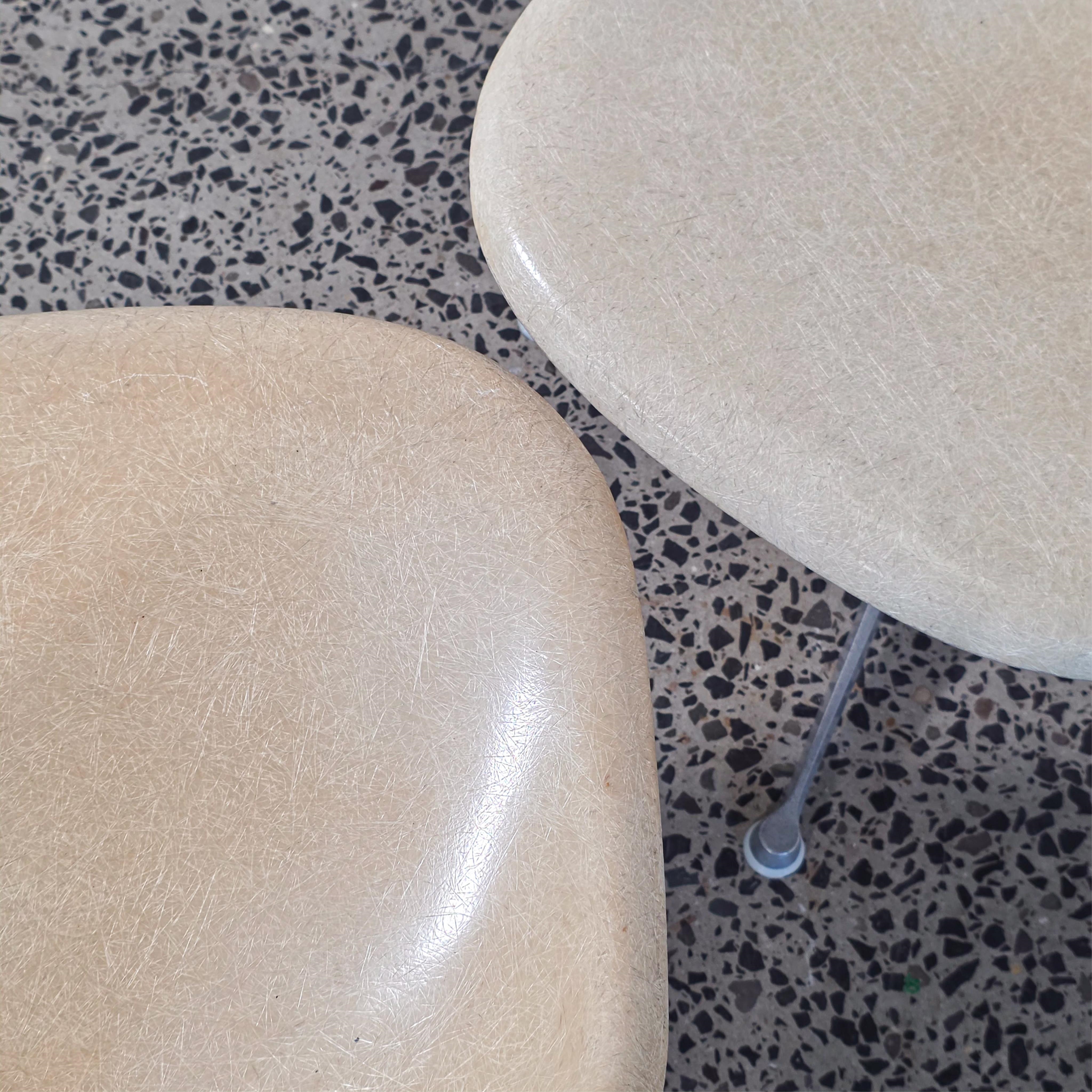 A pair of beige molded chairs on star-shaped bases against a plain wall.