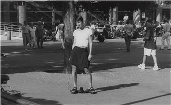 A black-and-white street scene featuring a person standing with headphones, surrounded by pedestrians and parked motorcycles.