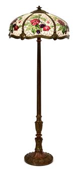A tall floor lamp with a stained-glass floral shade and an ornate dark metal base.