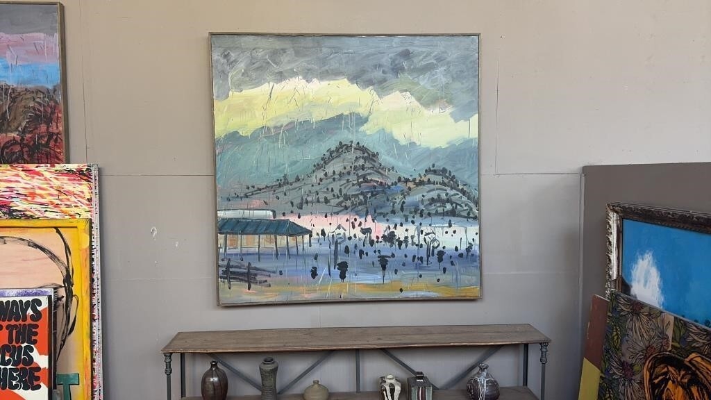 A landscape painting of a coastal town with a mountain and sea, displayed on a wall among other artworks.