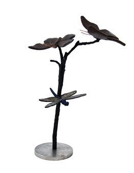 A dark metal sculpture of a stylized tree with leaves and a dragonfly, mounted on a circular base.