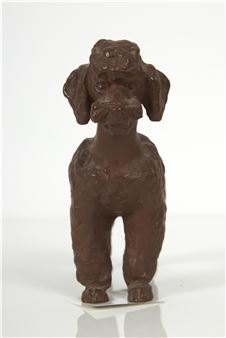 A sculptural figure of a poodle-like dog with a textured, chocolate-brown surface standing against a stark white background.
