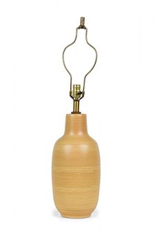 A minimalist table lamp featuring a light wood base and brass hardware against a stark white background.