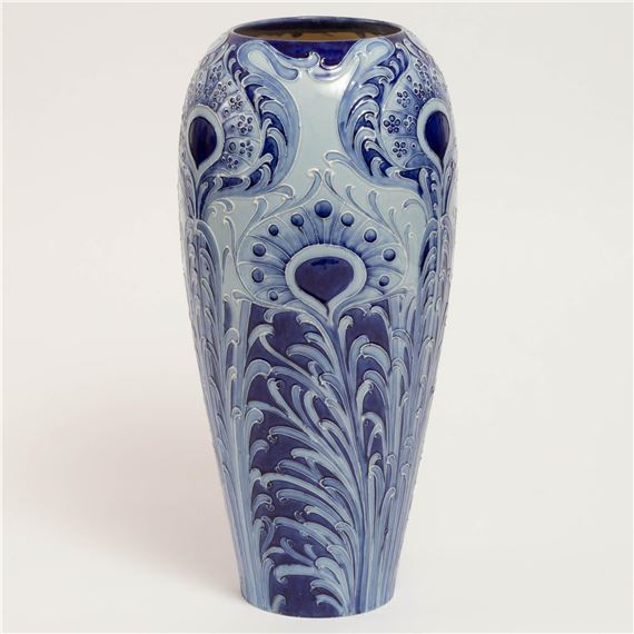 A blue ceramic vase featuring intricate floral relief patterns and a peacock feather motif.