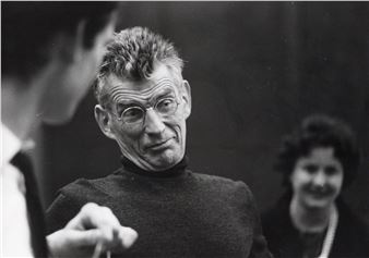 A black-and-white portrait of a man with glasses and a turtleneck, captured mid-conversation in a candid moment.