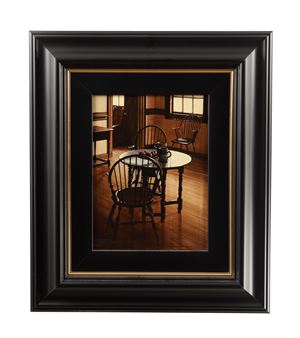 A framed still life of a wooden dining room with chairs and a table.