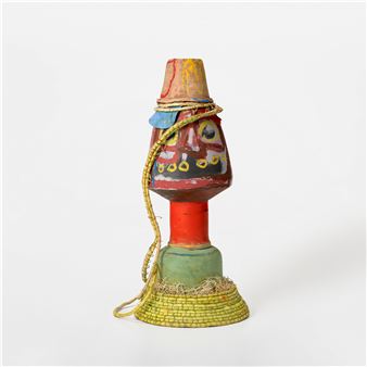 A colorful, multi-layered sculpture featuring a face-like central form and woven base.