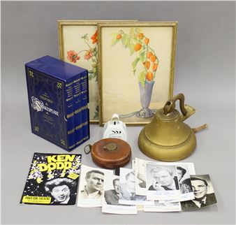 A still life arrangement of vintage items including books, framed art, and a brass kettle.