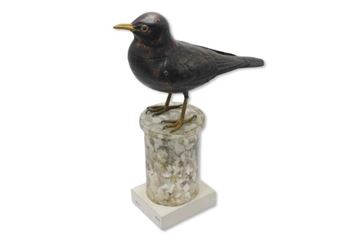 A dark bird sculpture perched atop a speckled stone pedestal.