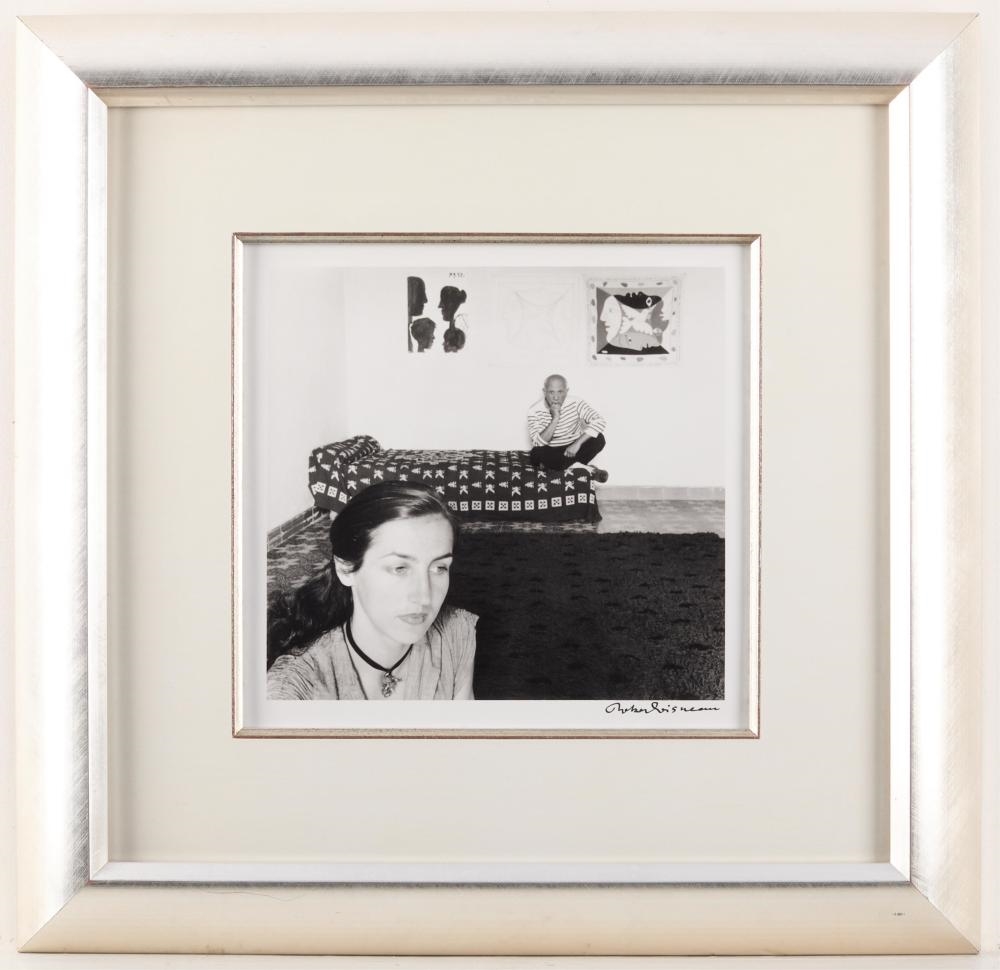 A black-and-white interior scene featuring a woman in the foreground and a man sitting on a patterned sofa in the background.