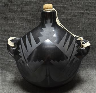 A black ceramic jug with etched geometric patterns and leather straps.